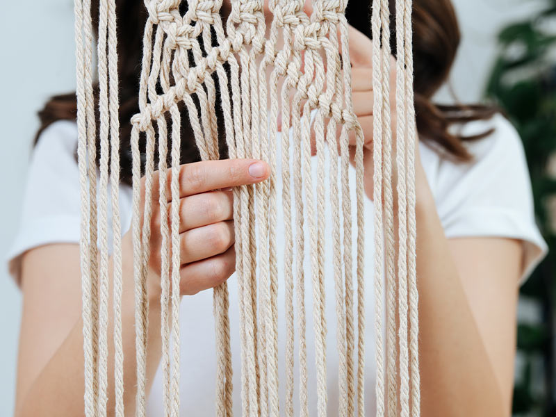 A person makes a macrame wall hanging