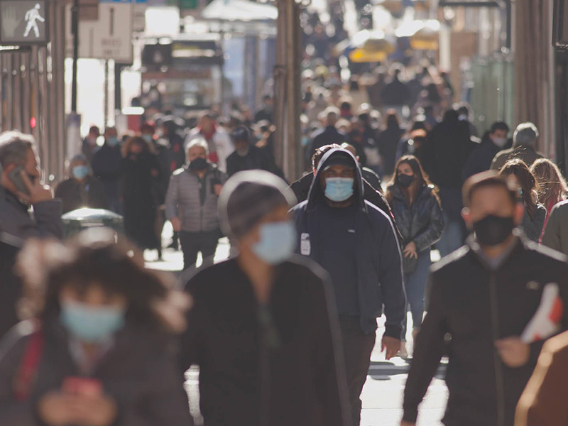 People wearing masks walk along a crowded city street.